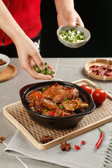 Chef garnishing braised goose with scallions in iron pot - traditional Asian cuisine cooking preparation