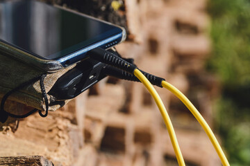 Smartphone charging from power bank outdoors with yellow USB cable on natural background.