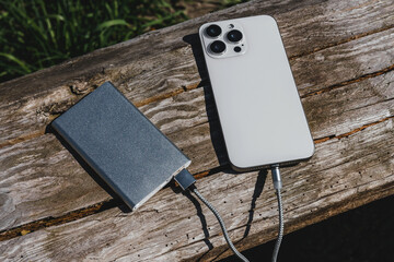 Smartphone charging with a powerbank on a rustic wooden surface. The natural wood texture complements the tech setup, ideal for outdoor and lifestyle themes.