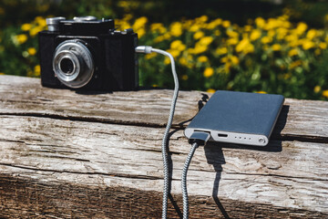 Vintage camera charging with a powerbank on a rustic wooden surface. The vibrant flower background enhances the outdoor photography tech scene, perfect for creative themes.
