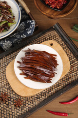 Asian dried meat jerky strips on wooden serving board with traditional table setting and red chili peppers