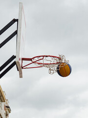 Basketball spinning on the rim during an outdoor game under cloudy skies