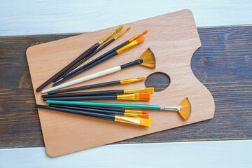 Art palette and different artistic paintbrushes on rustic table