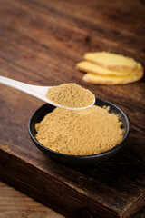 Ginger Powder Spice in Bowl with Wooden Spoon on Rustic Wood Background