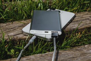 Charging from a Powerbank in nature: a modern smartphone and an external battery on a wooden log.