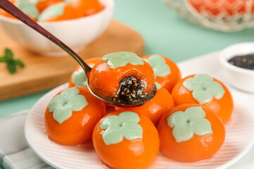 Traditional Asian persimmon dessert with green leaf decoration on white plate - festival food photography
