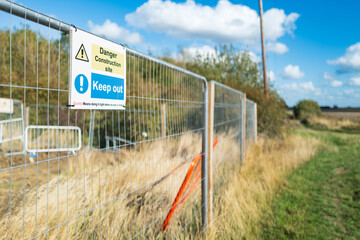 Shallow focus of a Keep Out sign seen attached to a metal fence at the perimeter of a new housing development site in the UK.  Land can be seen being cleared behind the fence.