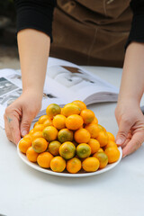 Fresh Kumquats from Rongan Guangxi China on White Plate with Hands Protection Display
