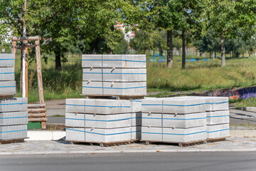 Stacks of large rectangular concrete blocks are strapped on wooden pallets at a construction site. The blocks are neatly aligned and ready for use.