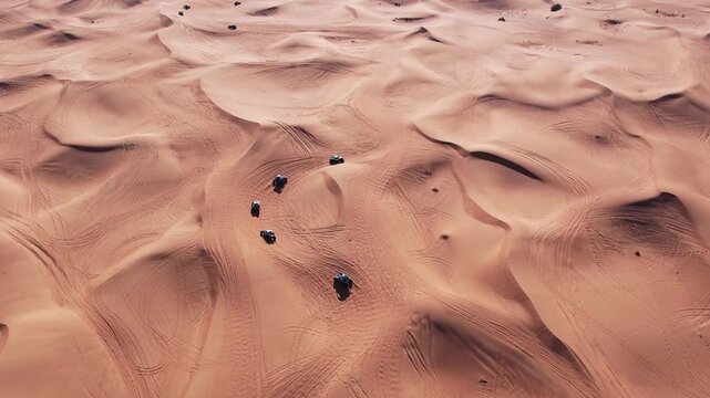 A drone flies over a caravan of buggies driving through the desert sand