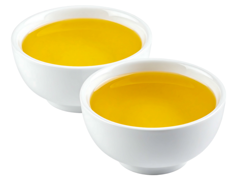 Two small, white, ceramic bowls filled to the brim with a vibrant, golden-yellow liquid, positioned closely together against a black background