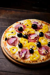 Pizza with salami, mozzarella cheese, black olives and pepper. Rustic wooden background. Soft focus. Copy space.	