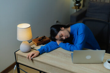 Young woman asleep face-down on her home office desk beside a laptop, exhausted from late-night overwork and burnout, needing rest amid stress and deadlines