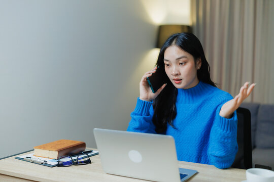 Young woman talks on her mobile phone, looking stressed while sitting at a desk with a laptop and documents, working remotely from her home office setup - Powered by Adobe