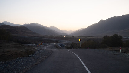 The winding road goes somewhere into the distance, mountain peaks are visible in the distance, twilight, evening panorama of the mountain crevice and the road ahead