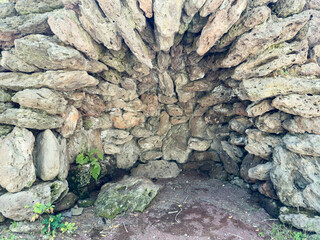 Small cave, cave made of stones, ancient abandoned place. A small stone structure with a hole in the middle. The hole is surrounded by rocks. The structure is located in a forest