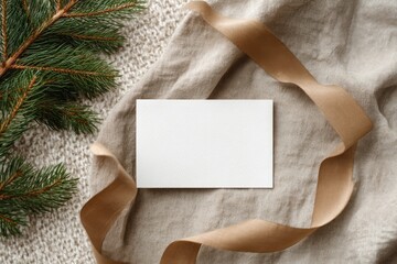 Blank card nestled on beige knit fabric with ribbon and pine branches