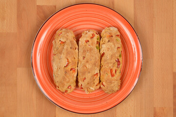 Three small loaves of freshly baked bread with chunks of red Macedonian sweet pepper, served on a textured orange plate