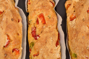 A detailed close-up of three freshly baked bread loaves with chunks of red Macedonian sweet pepper,...