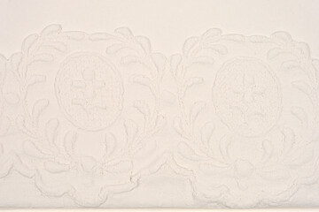 A close-up view of a delicate white plaster surface shows a detailed impression of a lace pattern, capturing the texture and ornamental design