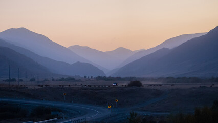 The winding road goes somewhere into the distance, mountain peaks are visible in the distance, twilight, evening panorama of the mountain crevice and the road ahead