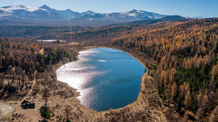 Autumn view of blue mountain lake with sunlight reflecting on surface of lake and snow-capped mountain peaks on background. Aerial drone view of Lake Kidelyu, Ulagansky Track Highway, Altai Mountains