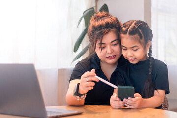 Mother and daughter share a moment while learning on a smartphone in a cozy indoor setting during the afternoon