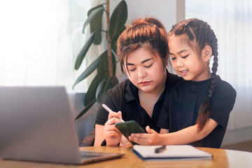 Mother and daughter working together on a digital device at home during daytime
