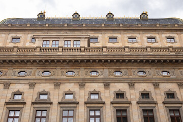 Historic building facade showcasing intricate architectural details, large windows, and decorative elements under a cloudy sky, representing classic urban design and heritage