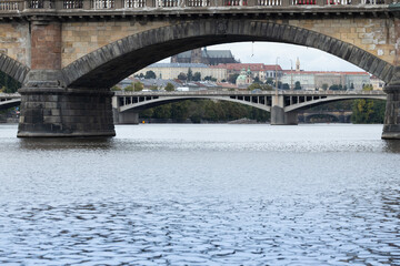 Architectural view of historic stone bridges spanning a river, with reflections on the water and a backdrop of city buildings under a cloudy sky showcasing urban beauty