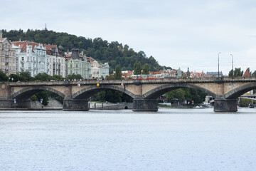 Naklejka premium Historic stone bridge spans a tranquil river, surrounded by lush greenery and elegant buildings, showcasing architectural beauty and serene waterscape