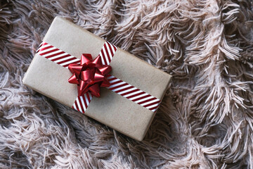Gift box in kraft paper with a red bow on a fluffy blanket.