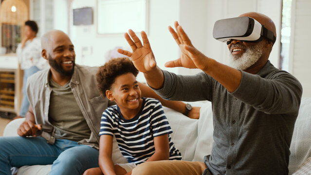 Grandfather Wearing VR Headset As Multi-Generation Male Family Sit On Sofa At Home Together