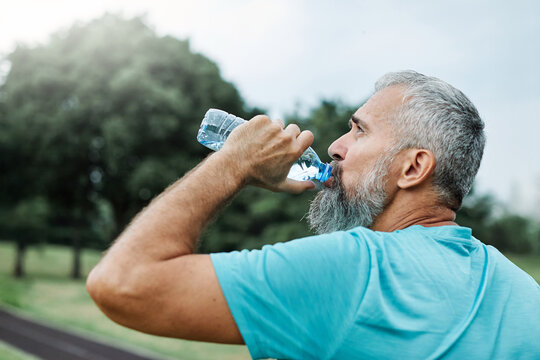 Smiling active mature mid aged coman jogging exercising and having fun and l taking a break drinking water in the park