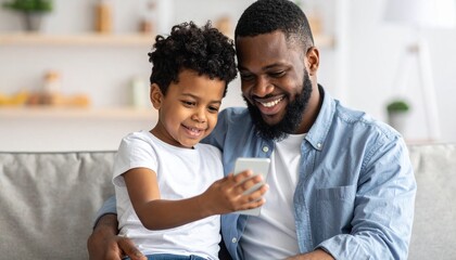 Fototapeta premium A young boy and his father looking at a mobile phone. Two generations learning technology together