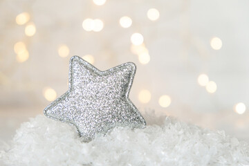 A sparkling Christmas tree ornament in the shape of a pentagonal star against a background of Christmas lights and snow.