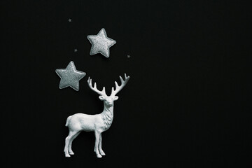A delicate reindeer figurine is surrounded by shimmering silver stars on a black background. Top view, space for text.