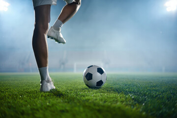 Naklejka premium Closeup of a soccer players legs and feet kicking a ball on a green field under bright stadium lights, showcasing the action and skill