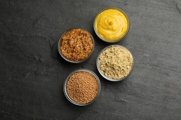 Different types of mustard on black table, flat lay