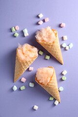 Cotton candy in waffle cones and marshmallows on violet background, flat lay