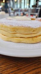 Close-up of delicious melt butter cream sugar powder with raspberry banana fruit pearl pancake triple layers on a wooden table in a stylish elegant Ginza Tokyo café, winter afternoon tea atmosphere