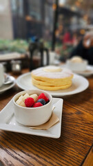 Close-up of delicious melt butter cream sugar powder with raspberry banana fruit pearl pancake triple layers on a wooden table in a stylish elegant Ginza Tokyo café, winter afternoon tea atmosphere