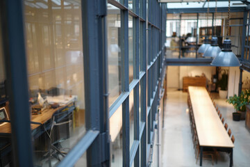 Obraz premium Modern openplan office interior with long conference table, desks, and industrialstyle lighting, viewed through a glass partition