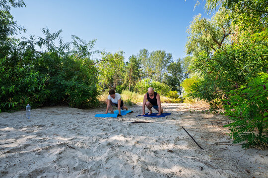 Couple exercising outdoors on sandy ground amidst lush greenery under a clear sky, embracing a healthy lifestyle and nature's tranquility. - Powered by Adobe