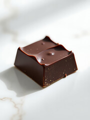 solitary richly textured dark chocolate square rests white marble surface illuminated soft overhead light subtle shadows