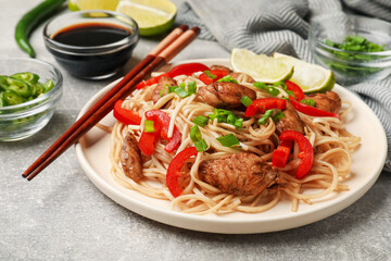 Tasty noodles with chicken, green onions and vegetables served on light grey table, closeup