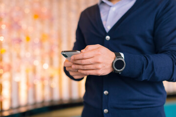 A man wearing a stylish navy cardigan is intently checking his smartphone, reflecting the contemporary habits of modern communication in our lives