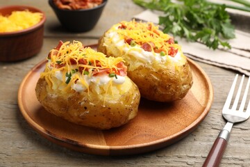 Tasty baked potatoes with sour cream, green onion, cheese and bacon served on wooden table, closeup