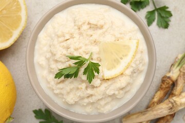 Tasty horseradish sauce with parsley, lemon slice and roots on light table, flat lay
