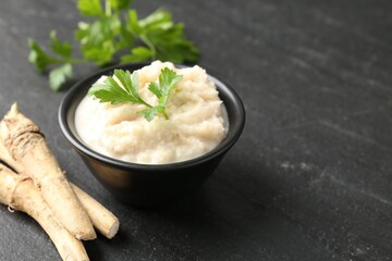 Tasty horseradish sauce with parsley and roots on black table, closeup. Space for text